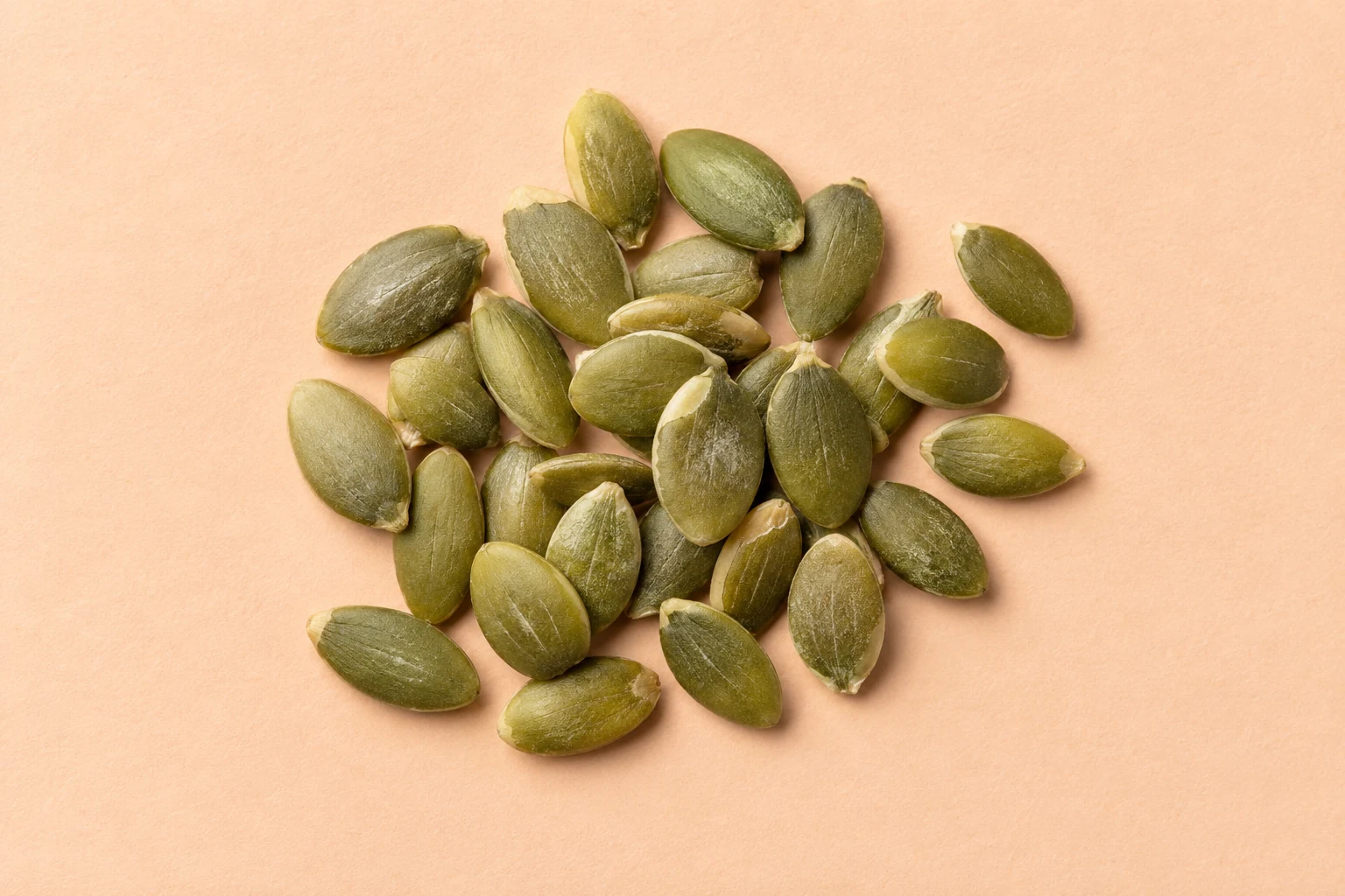 Shelled green pumpkin seeds on warm peach